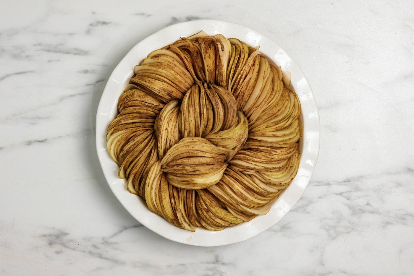 Sliced potato rounds stacked inside a deep dish pie plate in a circle