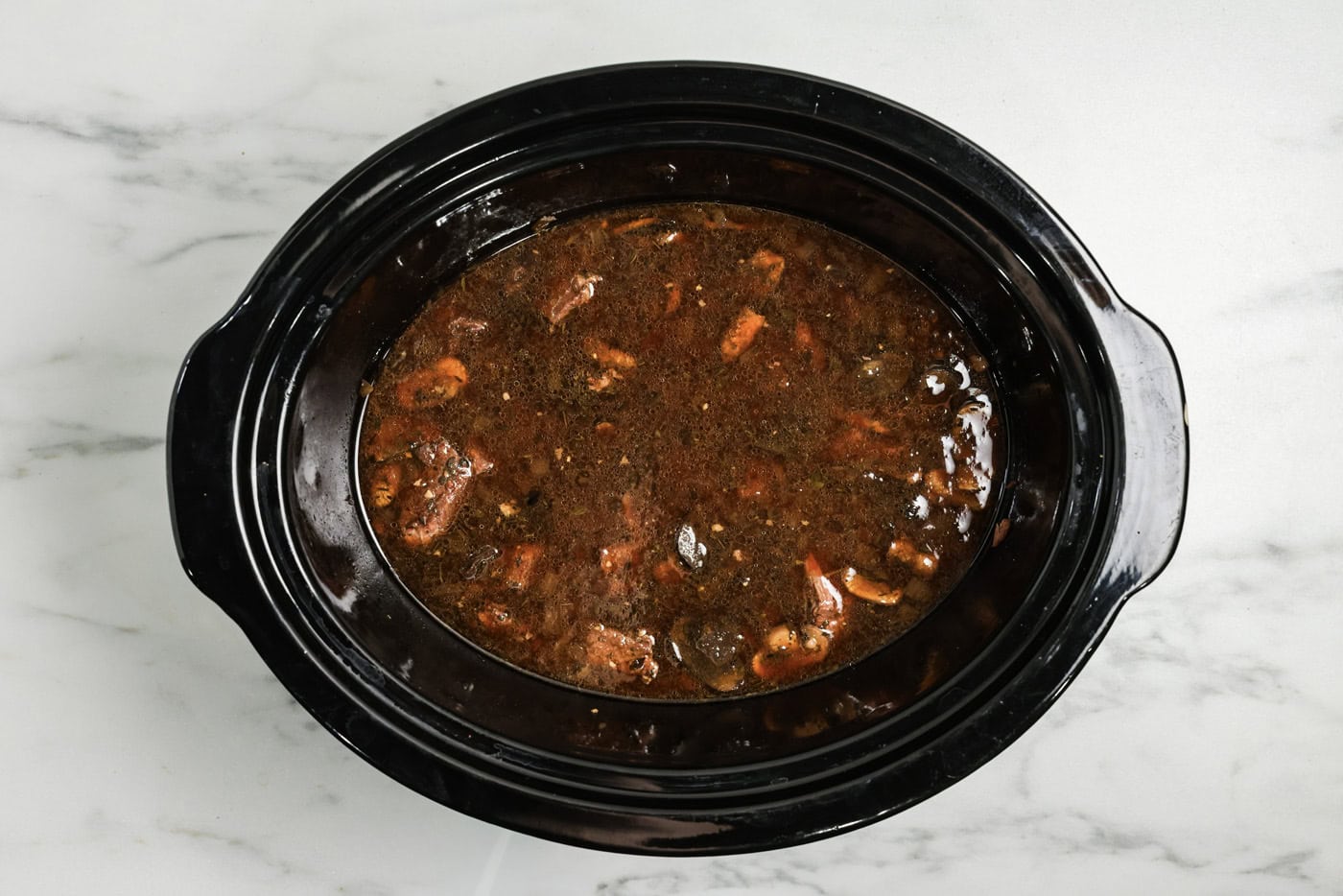 Beef broth added to crock pot with cubed beef, mushrooms, onions, and seasonings