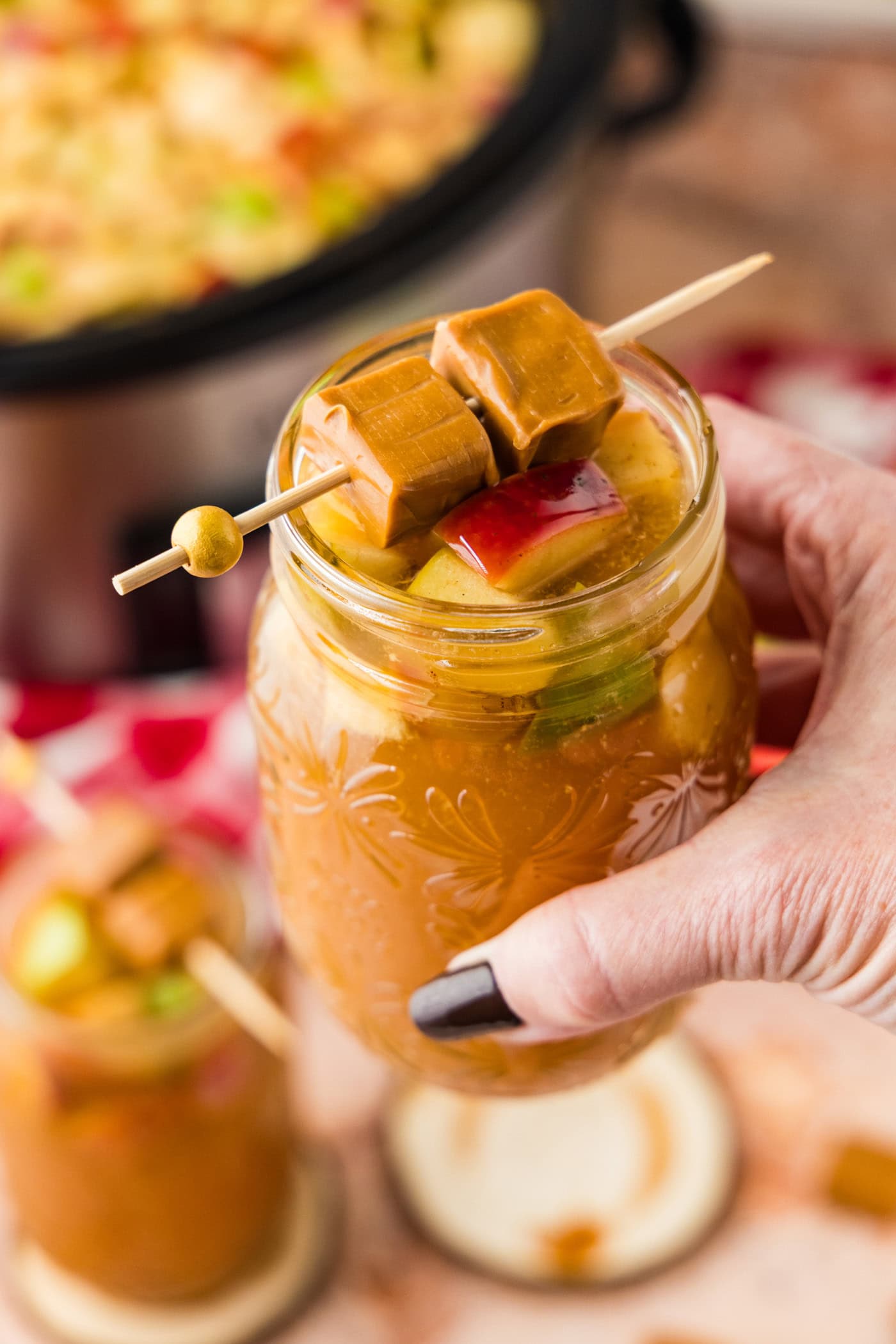 hand lifting a glass of Crockpot Caramel Apple Cider