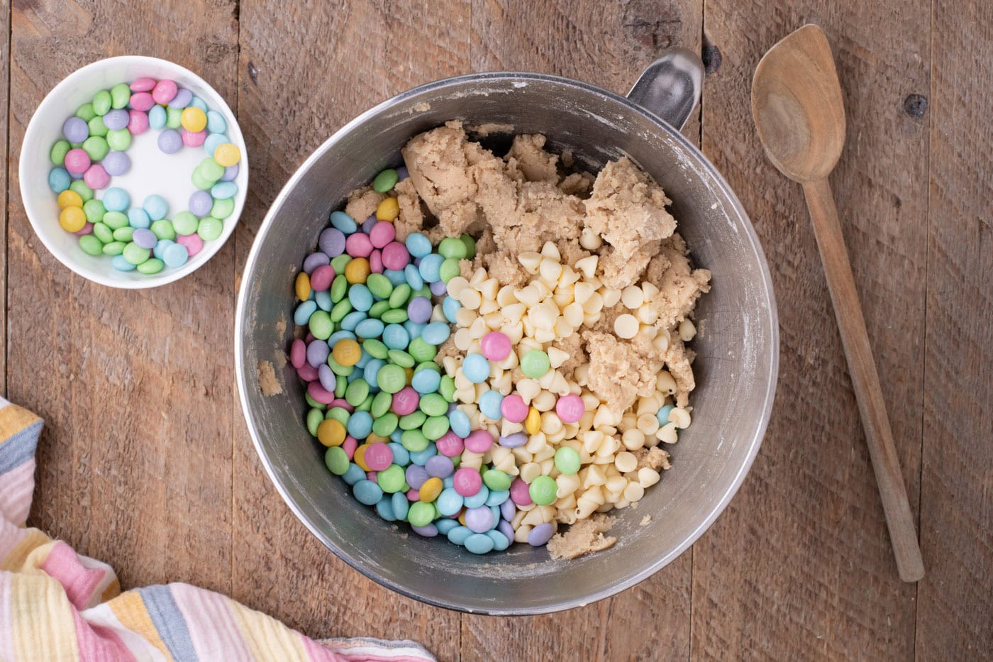 white chocolate chips and M&Ms added to cookie dough in a bowl