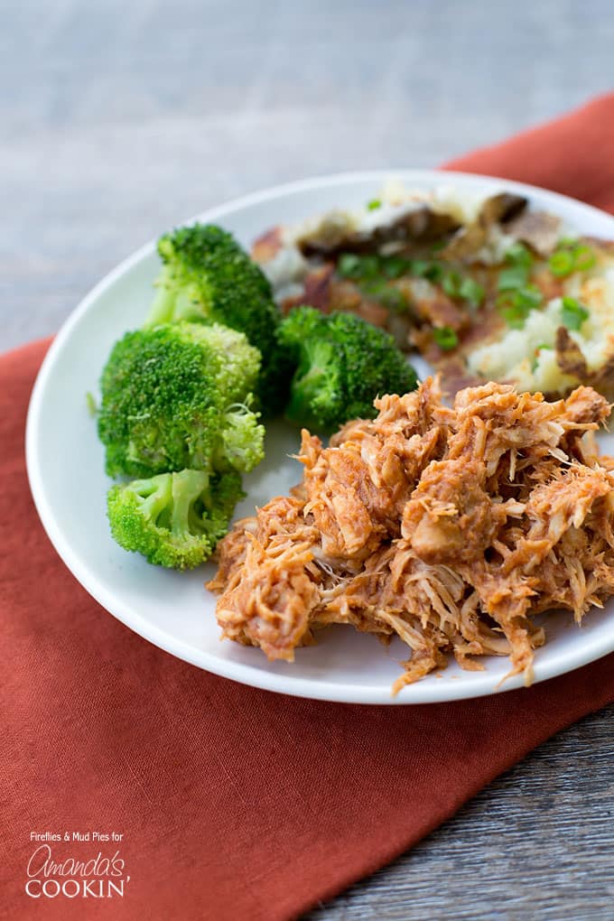 A close up photo of a plate of BBQ crockpot chicken and steamed broccoli.