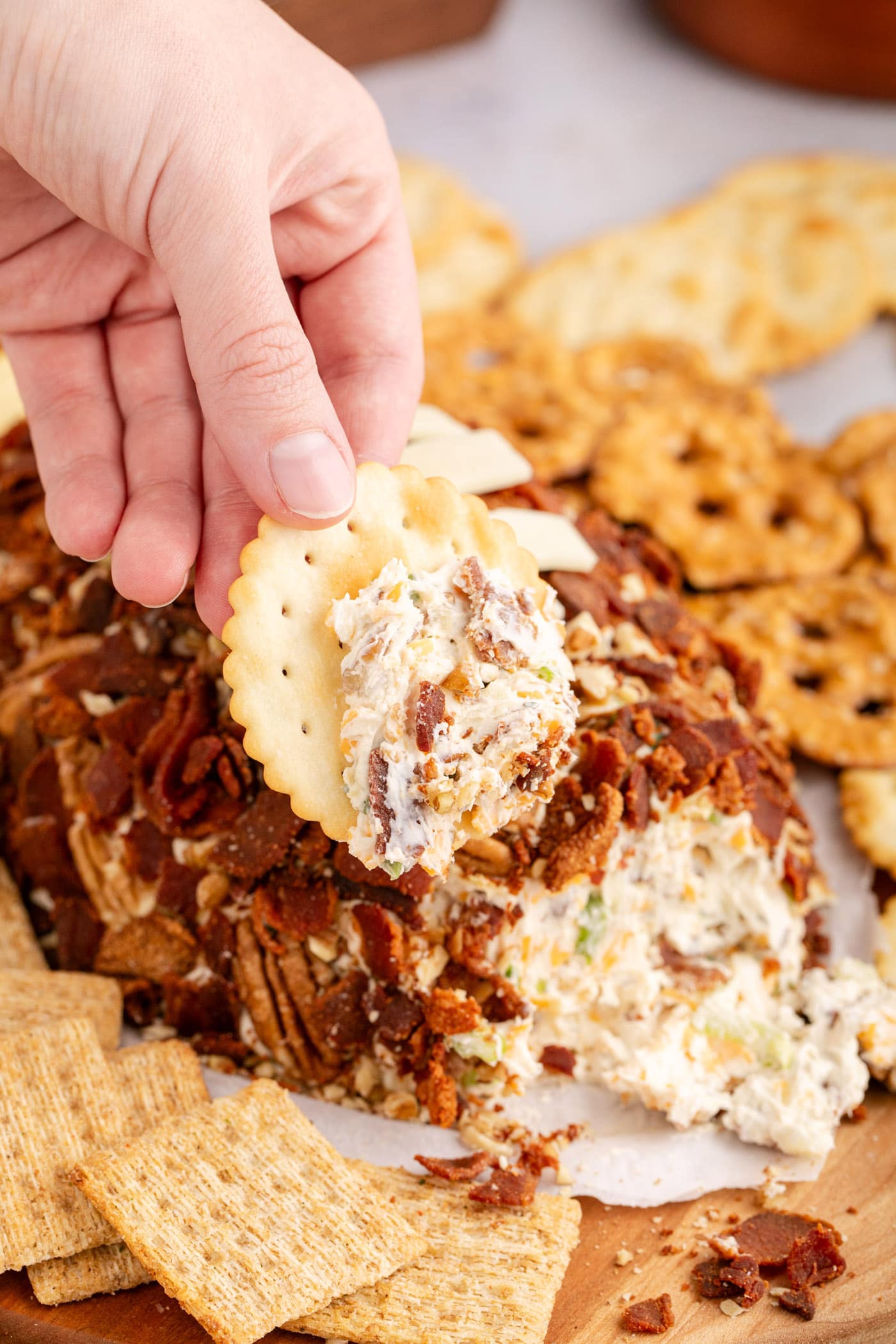 Hand holding a cracker with some cheese on it from the Football Cheese Ball