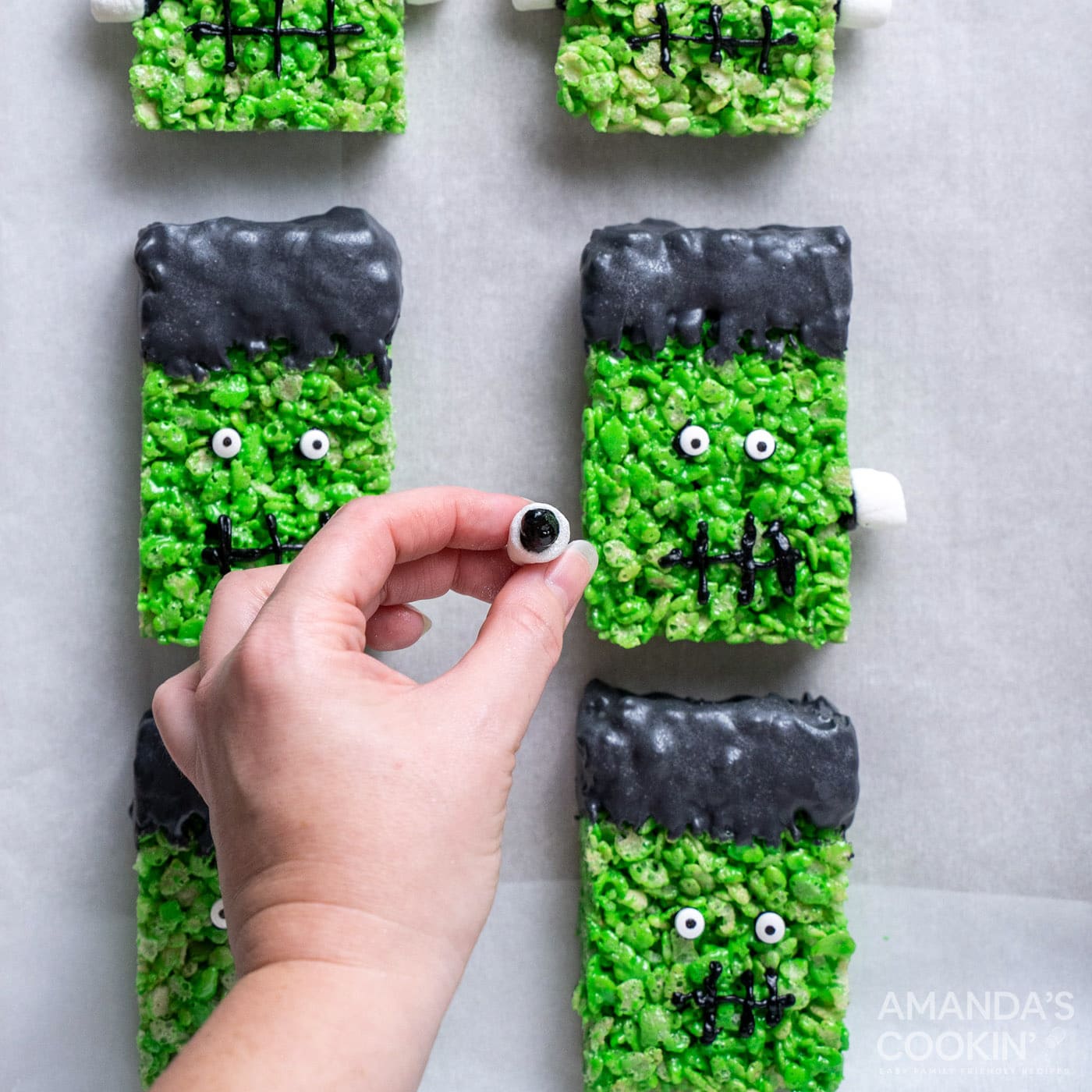 hand attaching mini marshmallows to frankenstein rice krispie treats