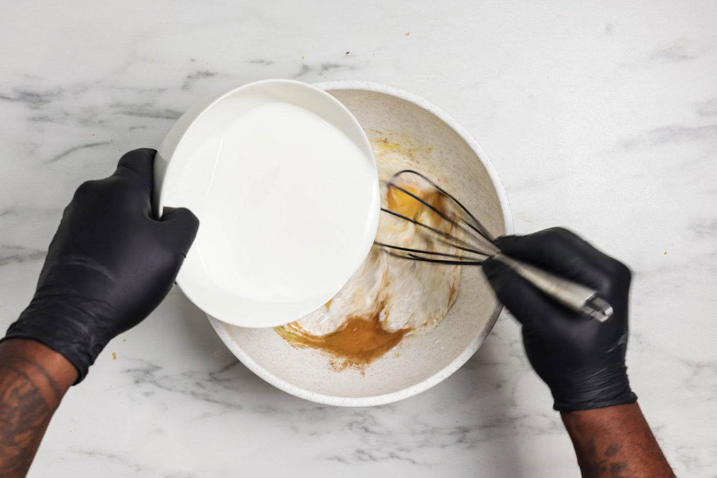 Hand pouring whole milk into bowl while whisking