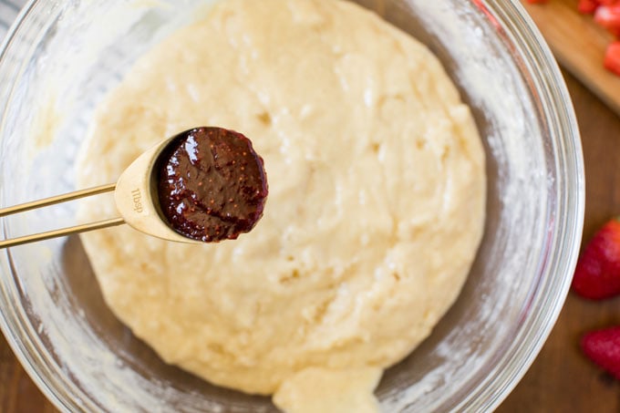 spoon of homemade strawberry jam hovering over bowl of muffin batter