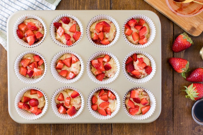 chopped strawberries on top of muffin batter in muffin tin