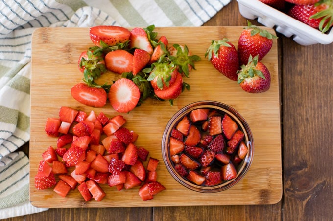 chopped strawberries and bowl of macerating strawberries on a cutting board