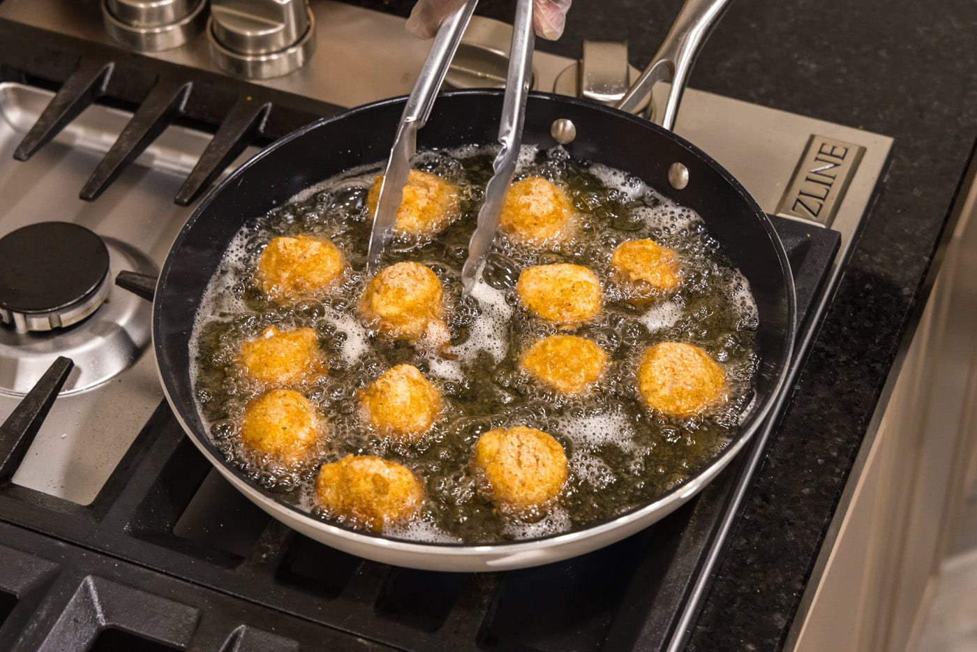 tongs turning scallops in a skillet of oil