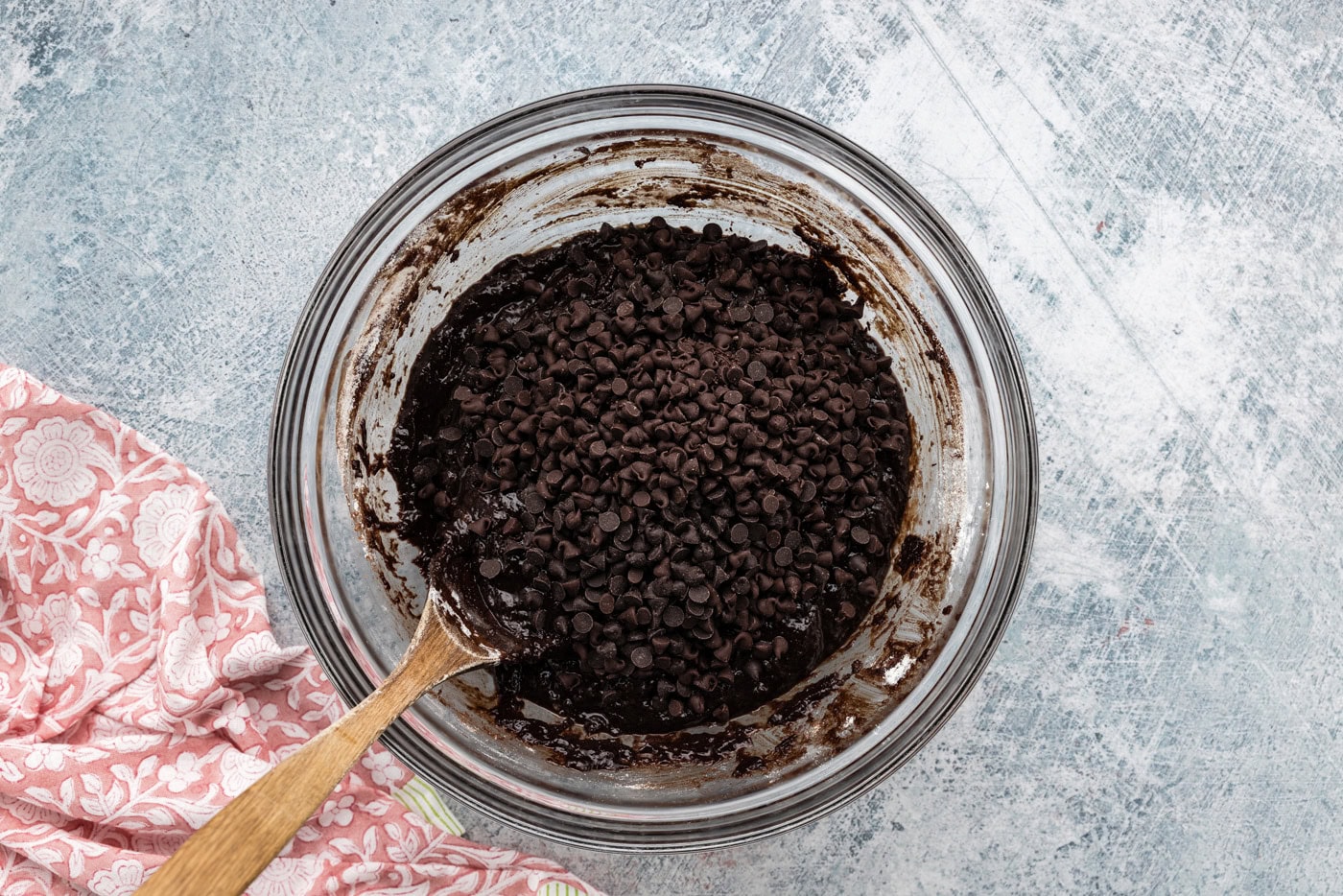 adding chocolate chips to espresso brownie batter in a bowl with a wooden spoon