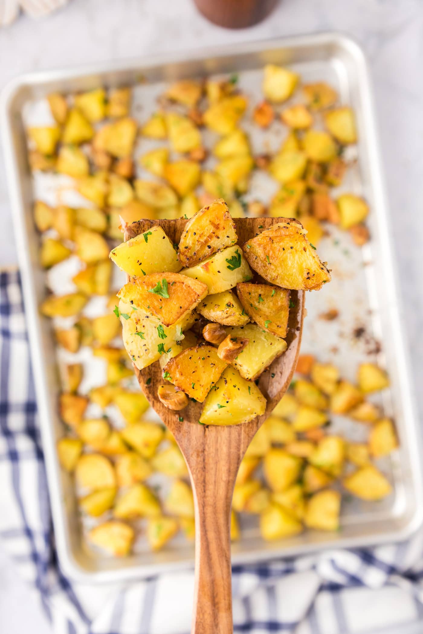 Spatula of Garlic Roasted Potatoes held over a pan of Garlic Roasted Potatoes