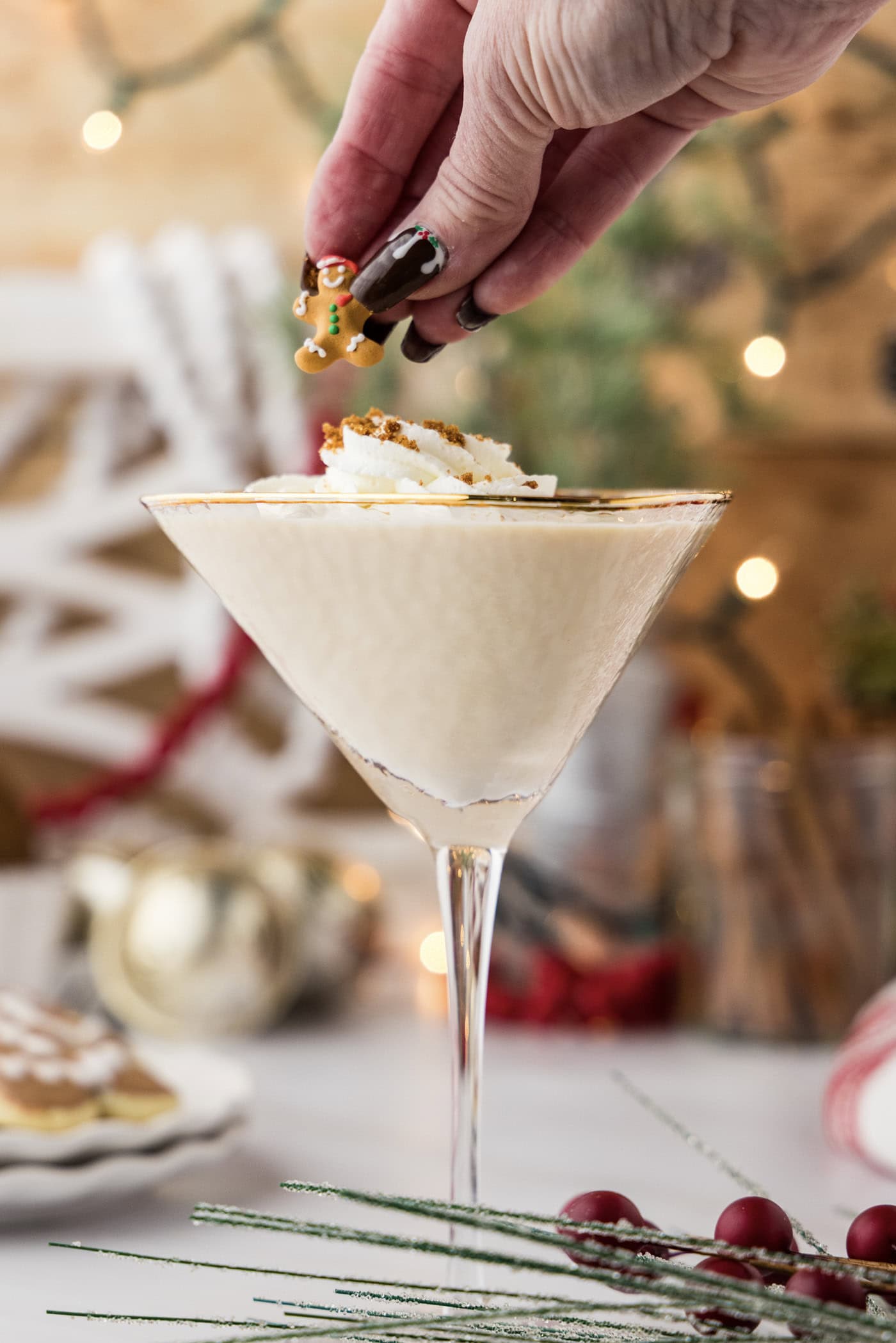 hand adding a gingerbread cupcake topper as garnish over whipped cream topped gingerbread martini