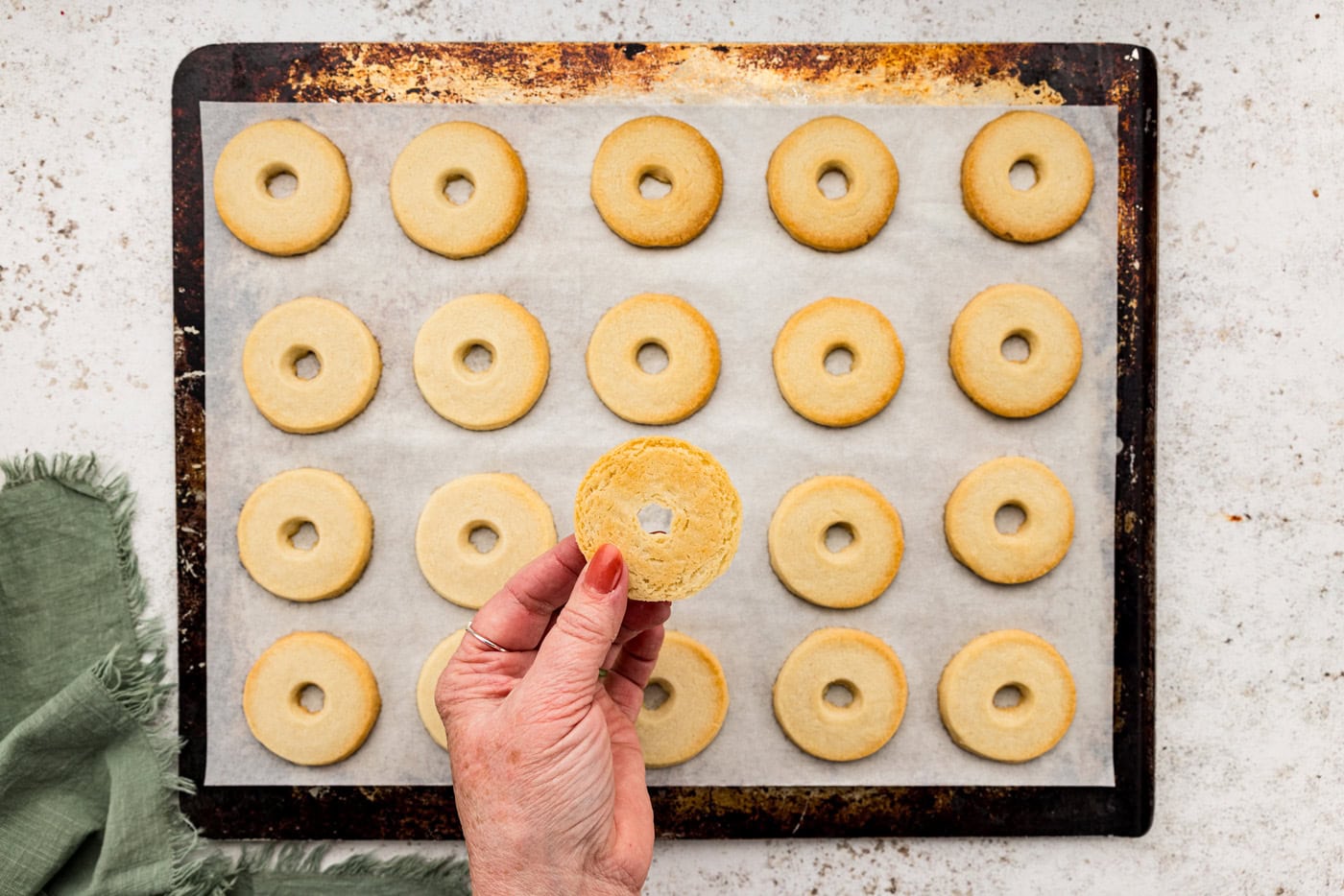 Hand holding baked shortbread cookie round over top baking sheet