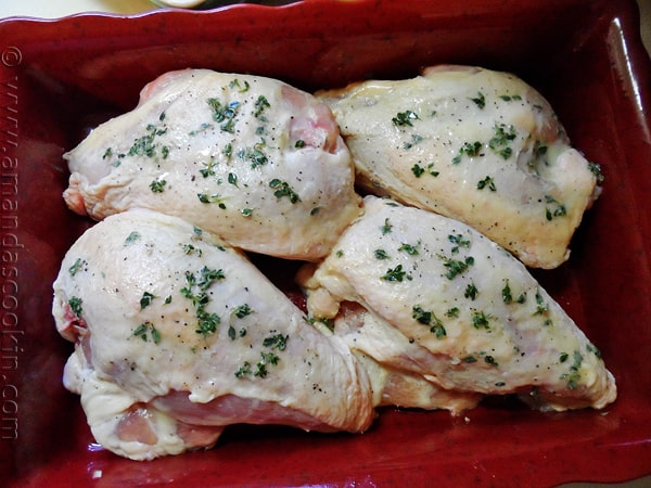 An overhead photo of chicken breasts in a red roasting pan topped with fresh lemon thyme leaves.