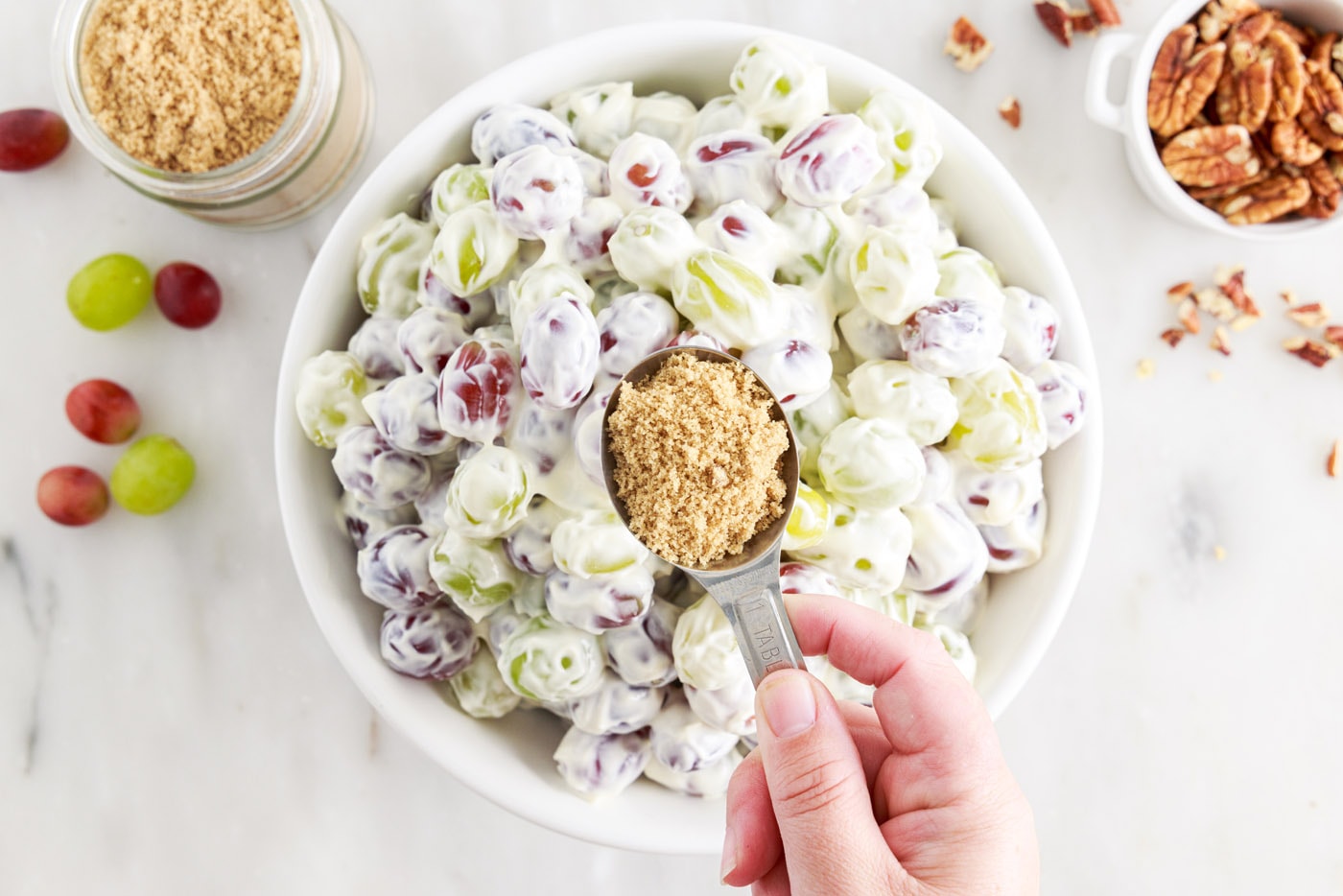 holding brown sugar over bowl of grape salad