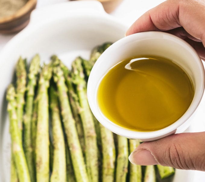 hand holding dish of olive oil with asparagus in the background