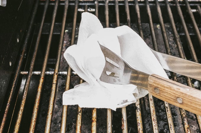 tongs holding paper towel over grill grates