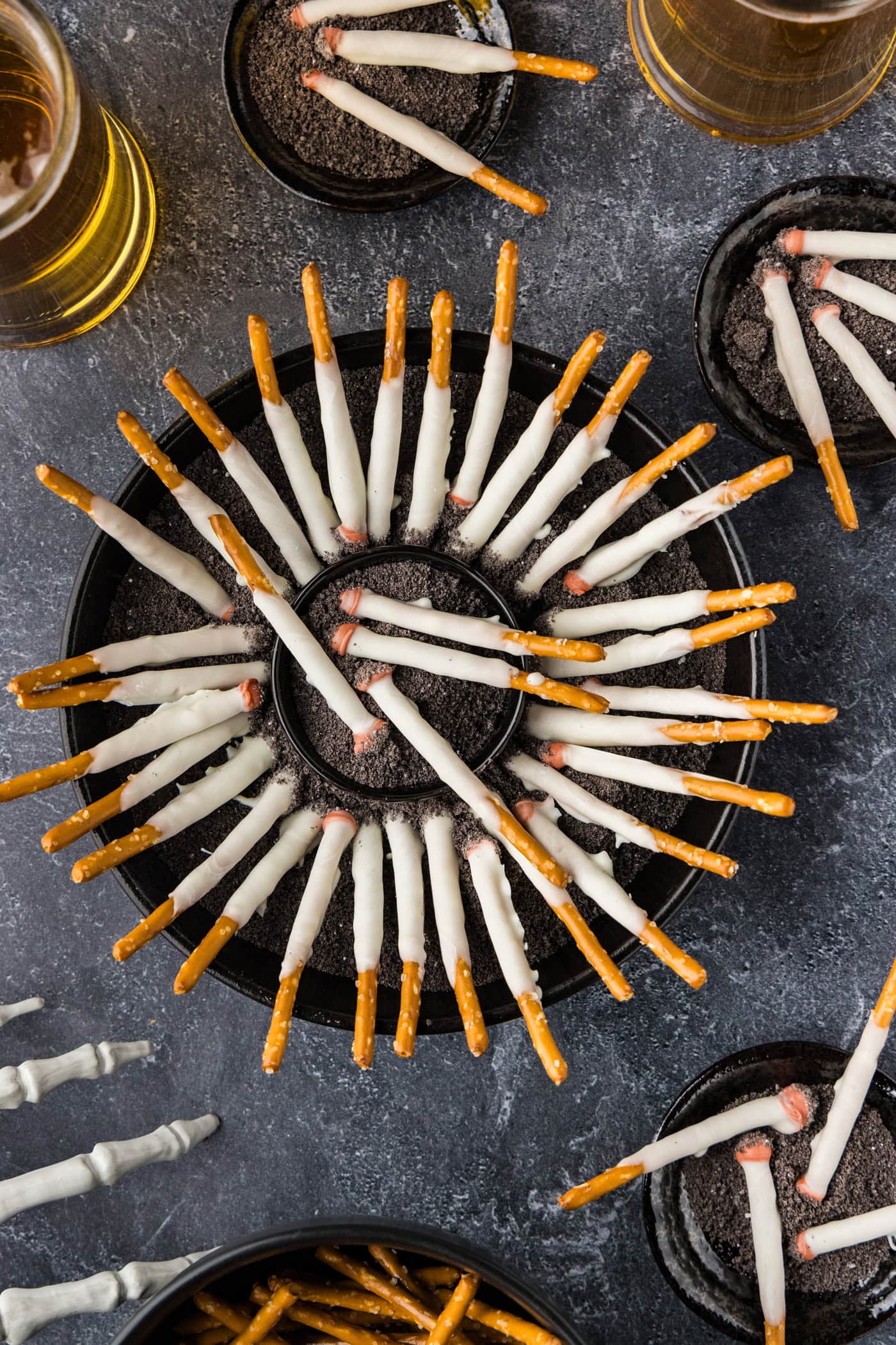 overhead view of Halloween Cigarette Pretzels on a table with drinks and a skeleton hand