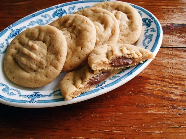A close up of a Hershey drop stuffed peanut butter cookie split in half on a plate with whole cookies in the background.