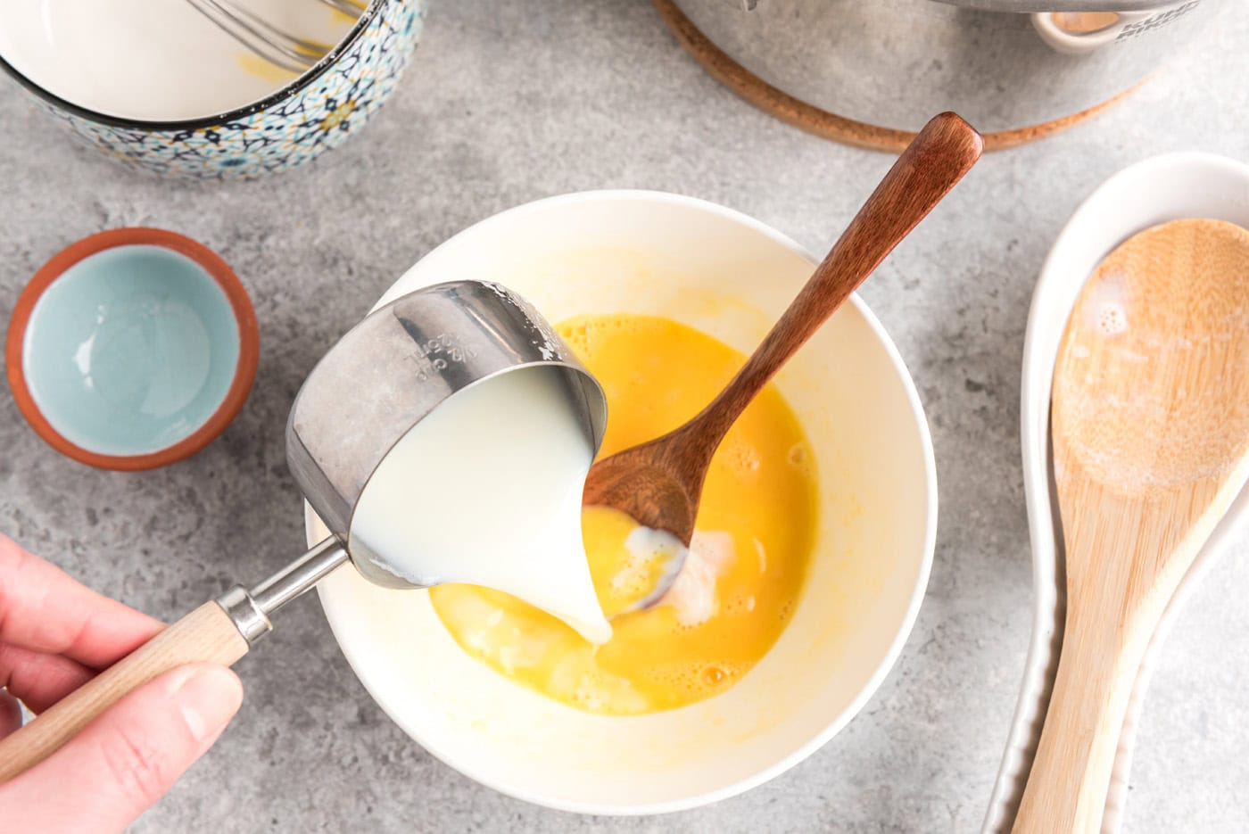 pouring milk into bowl of beaten eggs