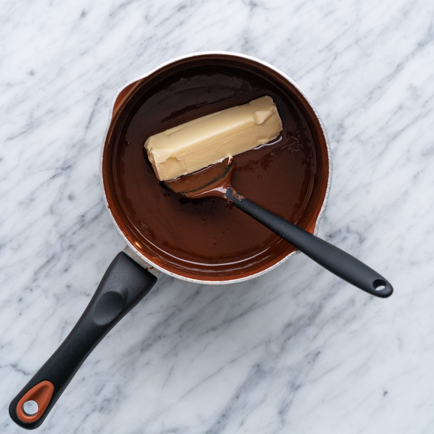 adding butter to hot fudge in a pot