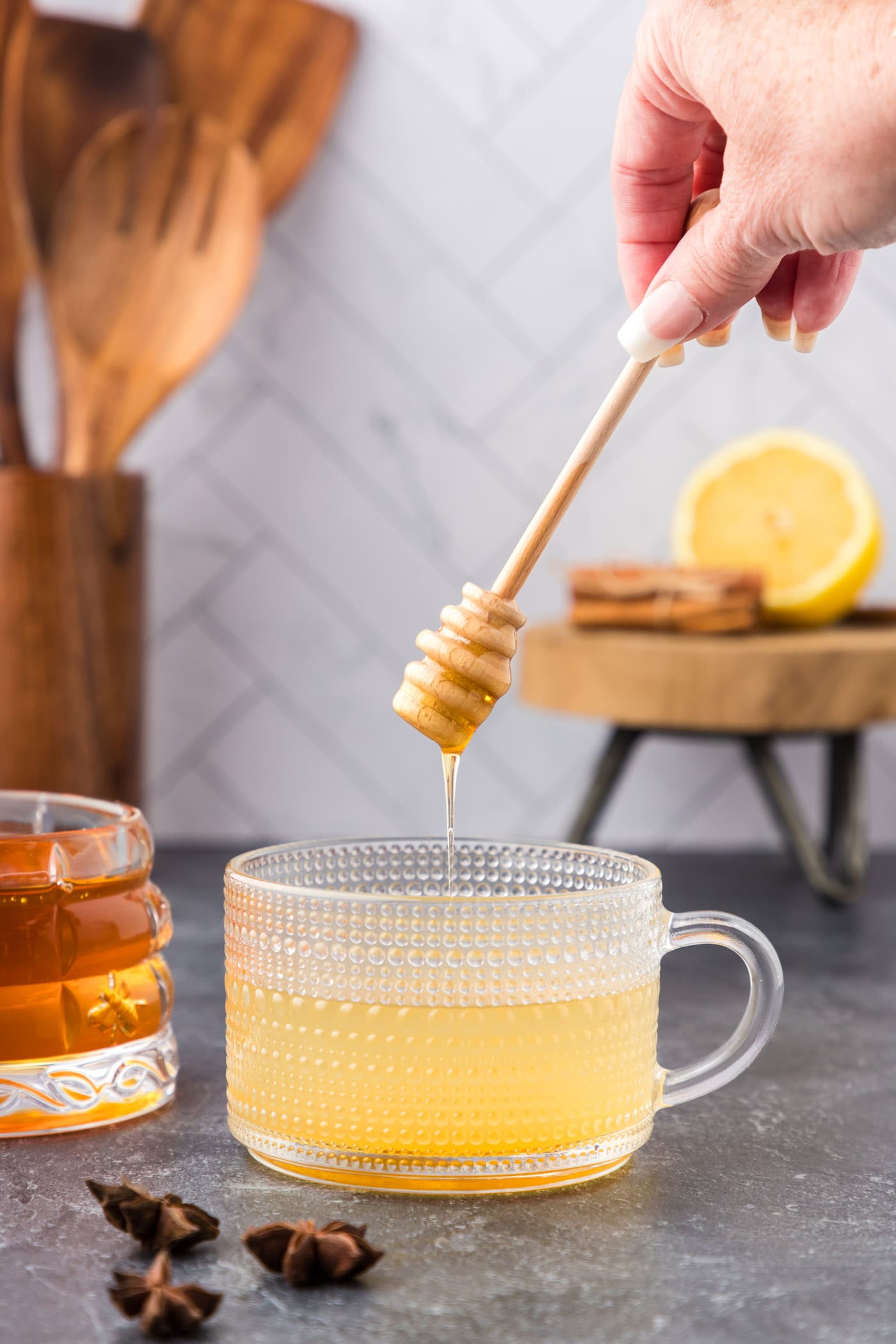 adding honey to glass with whiskey, water, and lemon juice