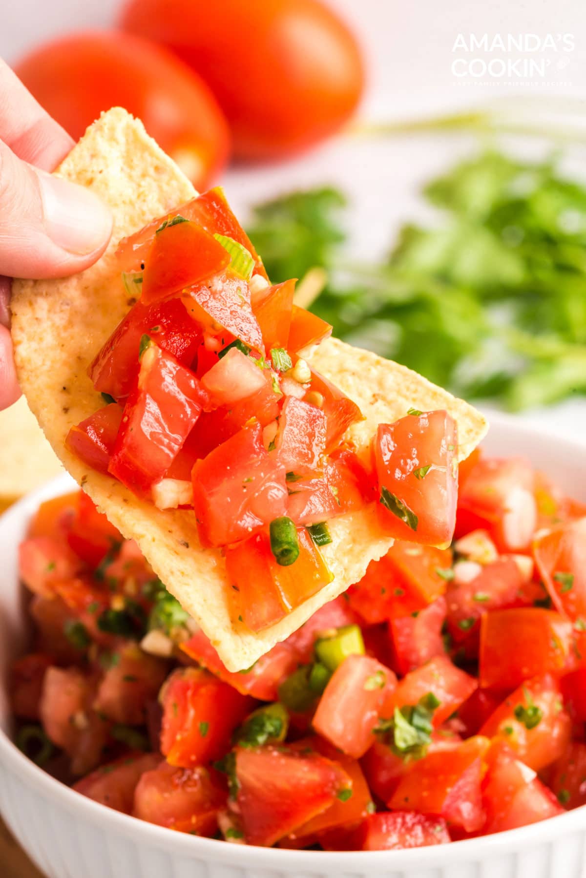 hand lifting tortilla chip with salsa fresca on it