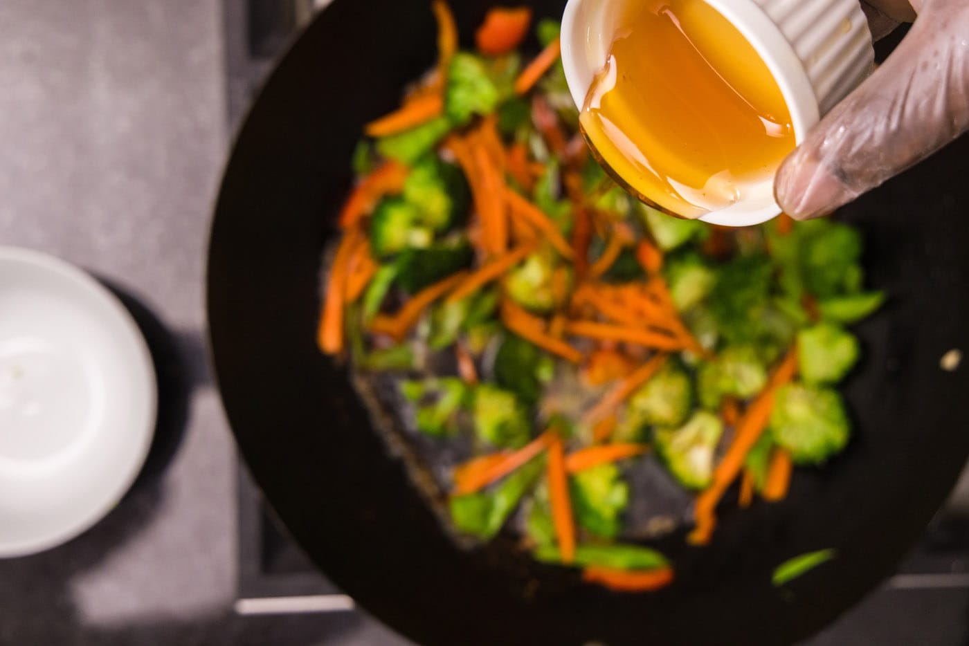 pouring honey into wok with vegetables