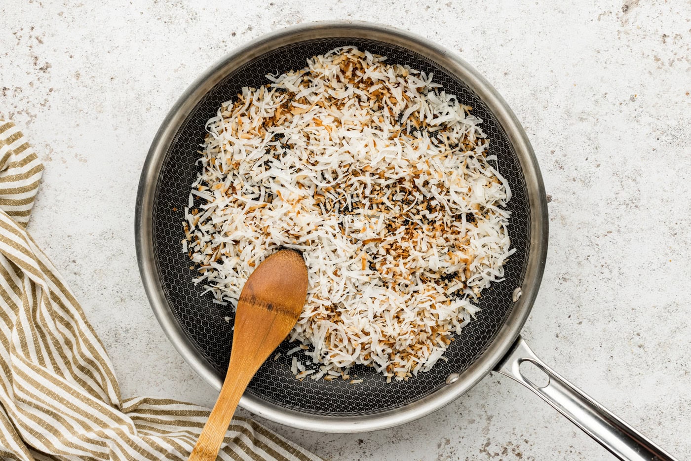 toasted shredded coconut in a skillet with a wooden spoon