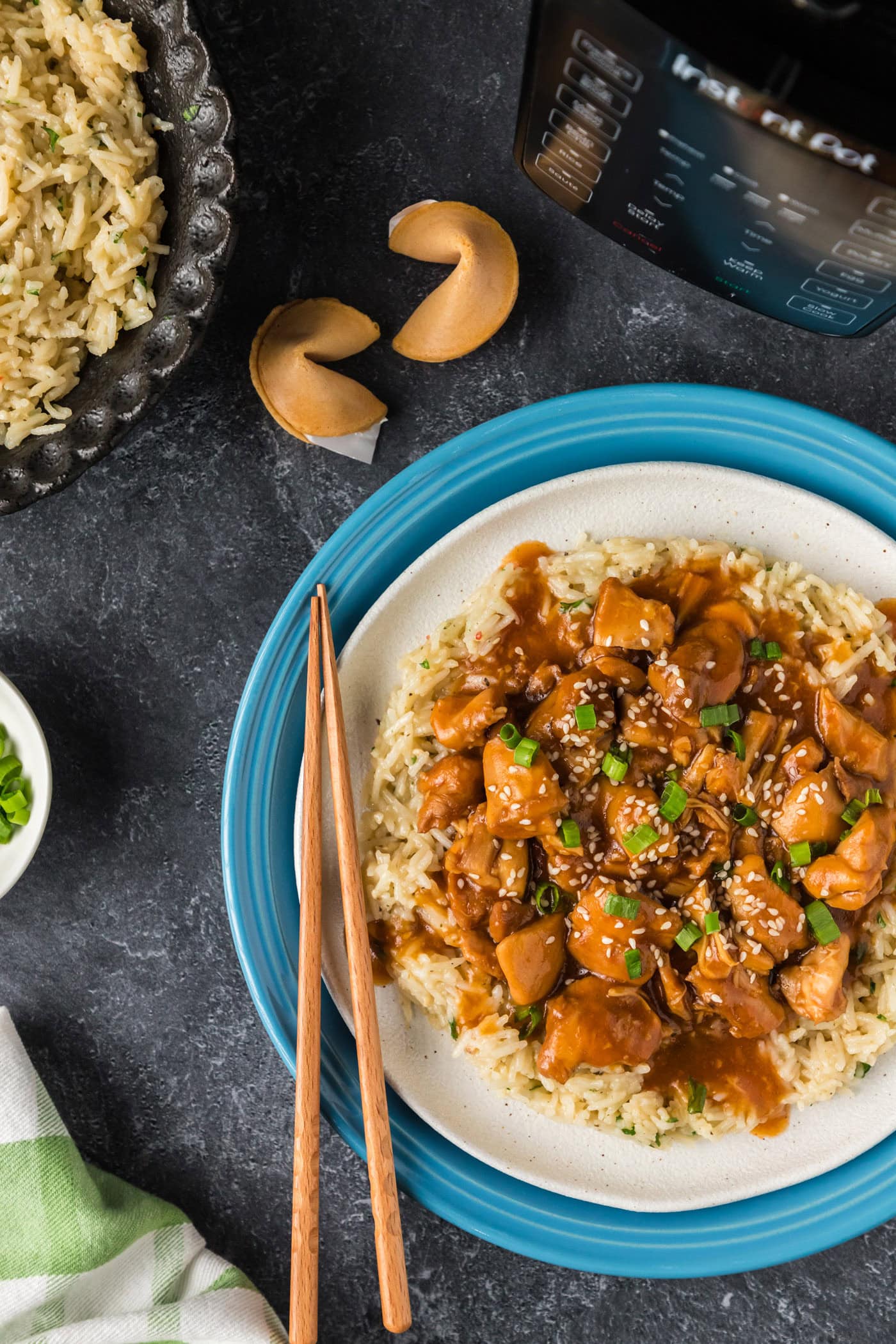 Half a plate of Instant Pot Bourbon Chicken over rice with fortune cookies in the background