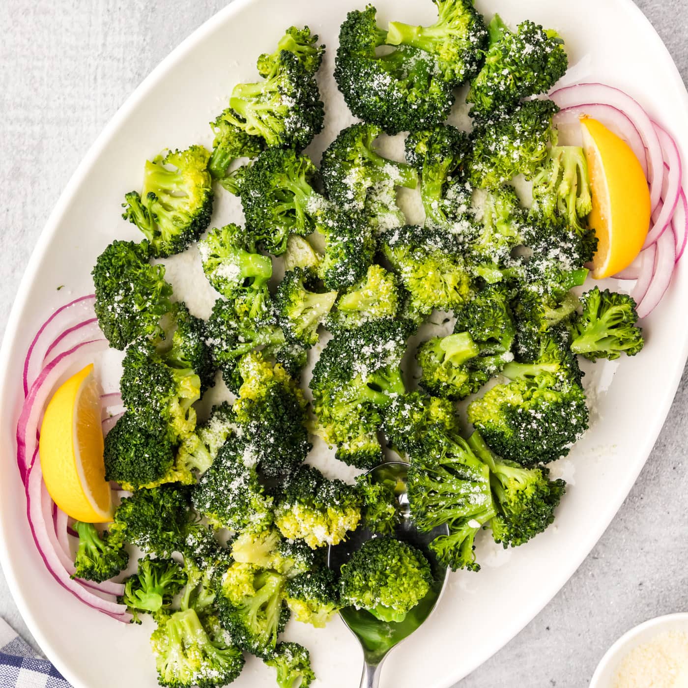 Instant Pot Broccoli on a white platter with onions and lemon wedges