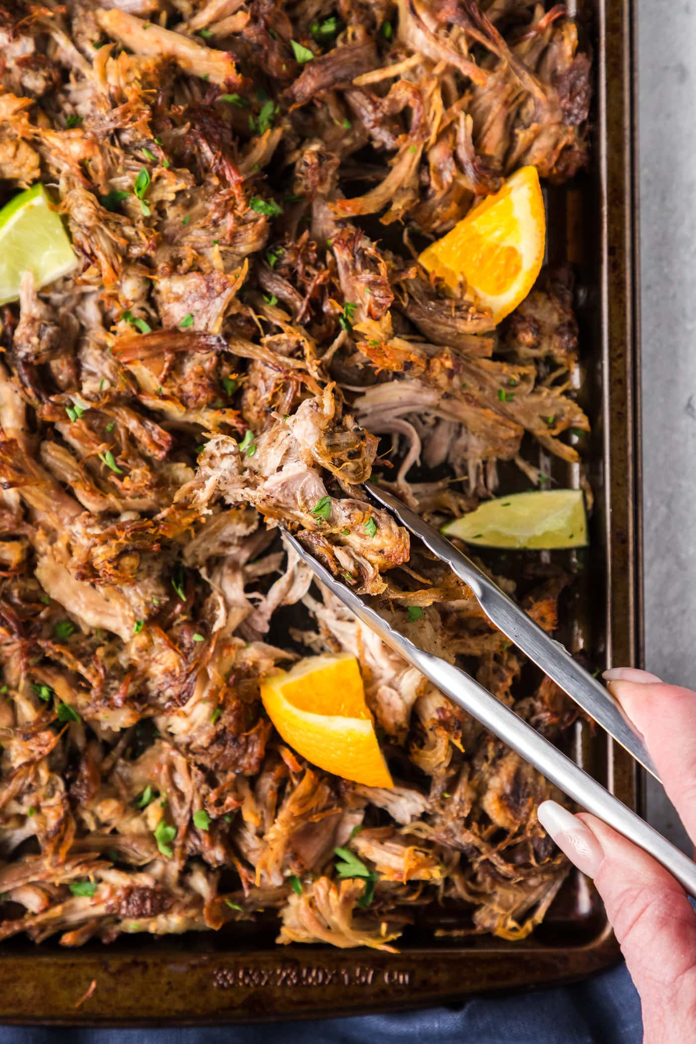 Tongs picking up Instant Pot Carnitas from a sheet pan