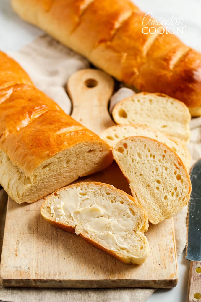 loaf of Italian bread on cutting board, slice of bread with butter