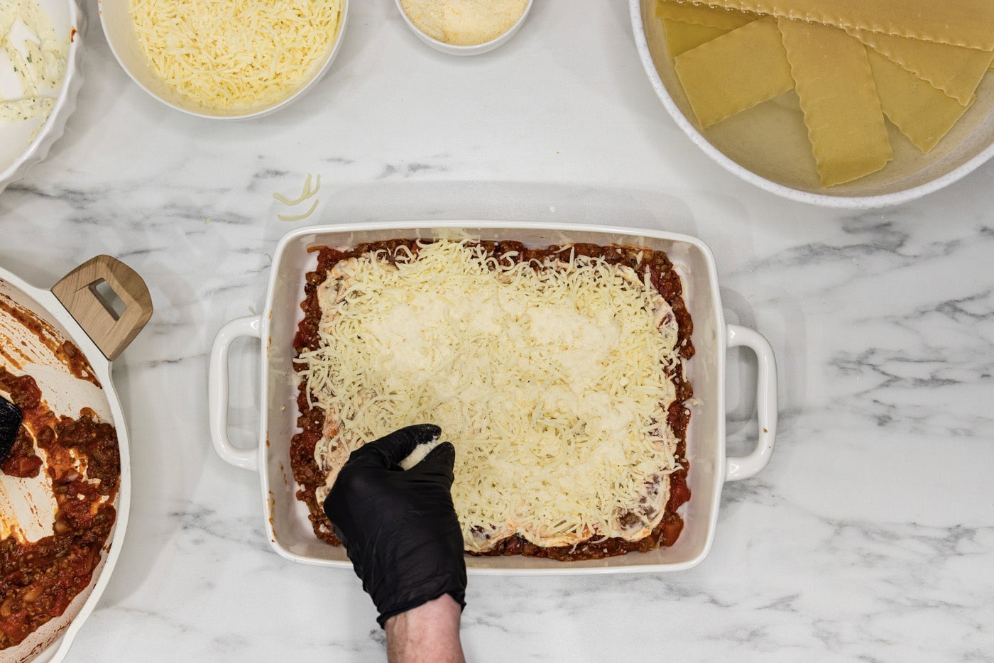 hand sprinkling shredded cheddar cheese and parmesan on top of lasagna