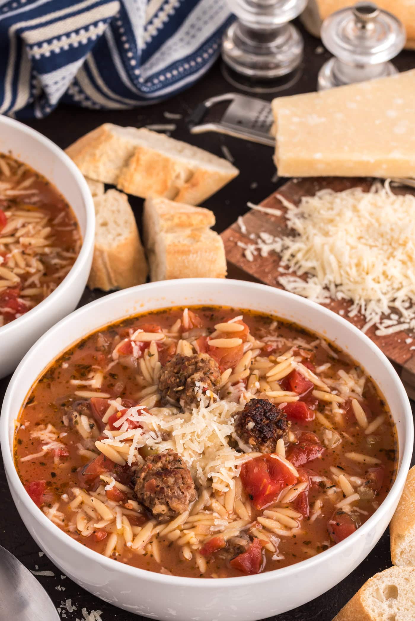 Two bowls of Italian Sausage Tomato Orzo Soup with bread and cheese in the background