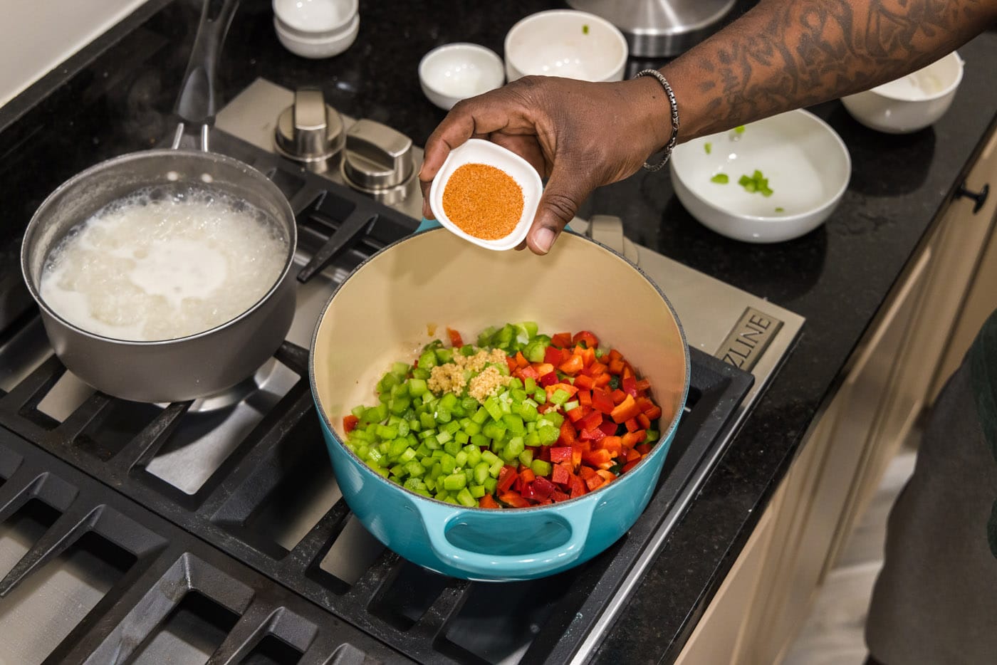 hand adding cajun seasoning to bell pepper, celery, onion, and garlic in a dutch oven