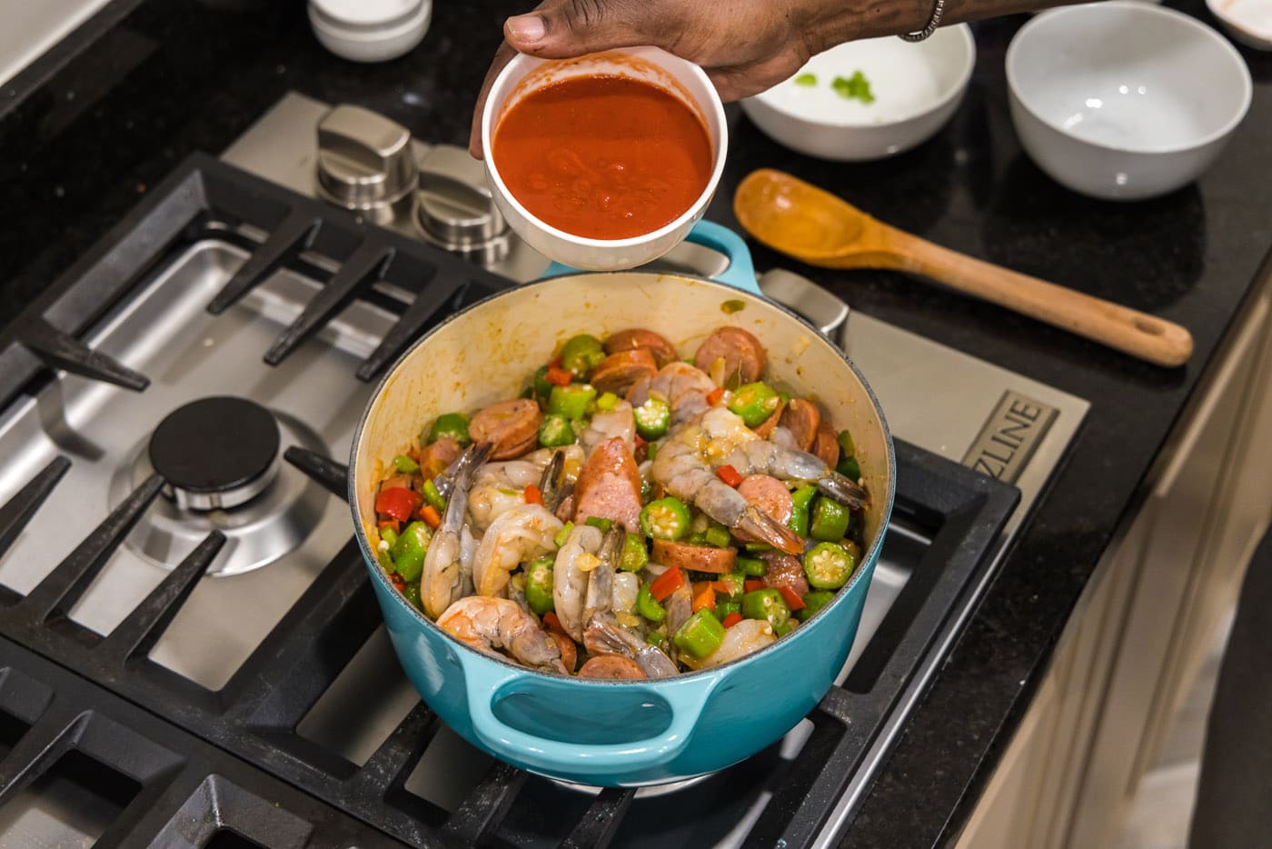 tomato sauce over pot with shrimp, sausage, and vegetables