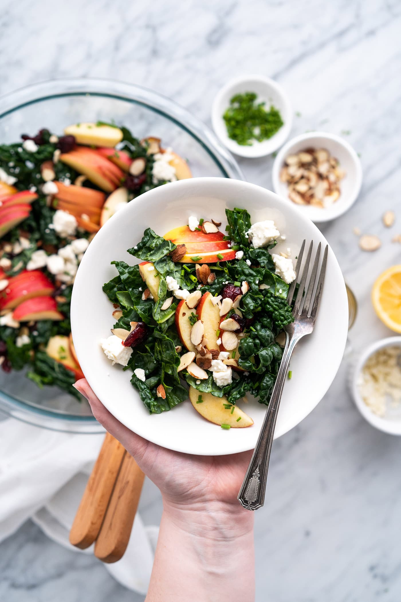 Singe serving of Kale Salad in a bowl being held over the batch of Kale Salad