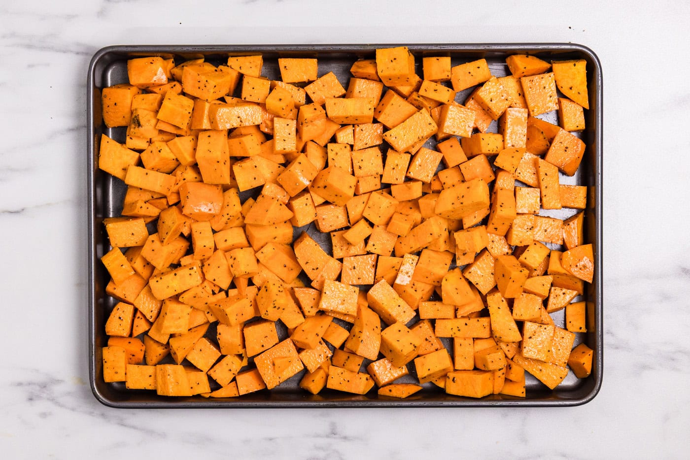 seasoned and oiled cubed sweet potatoes on a baking sheeet
