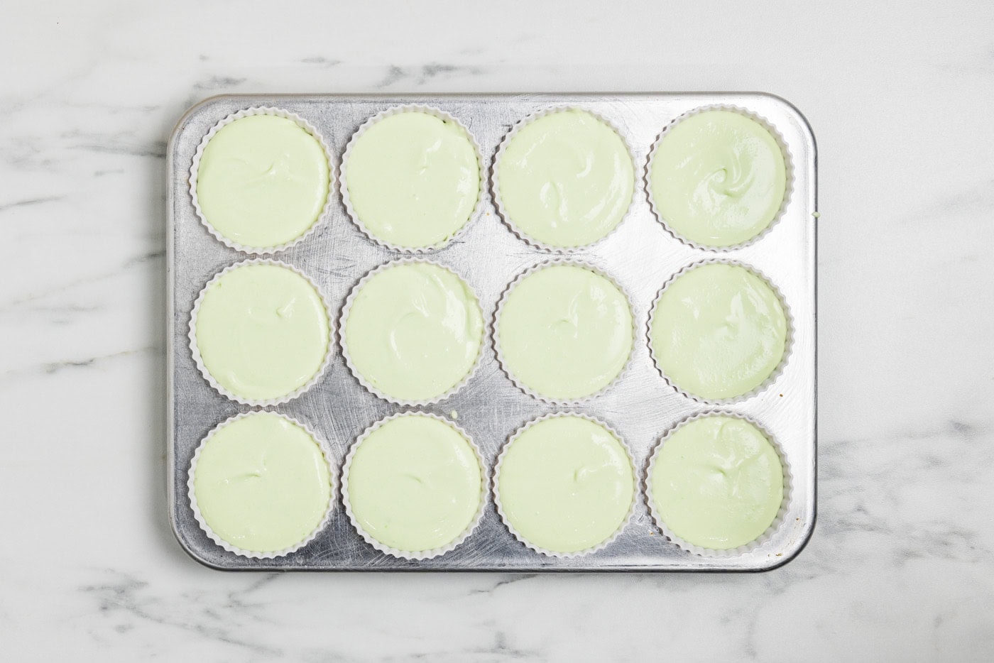 overhead photo of cheesecake mixture in silicone baking cups inside a muffin pan