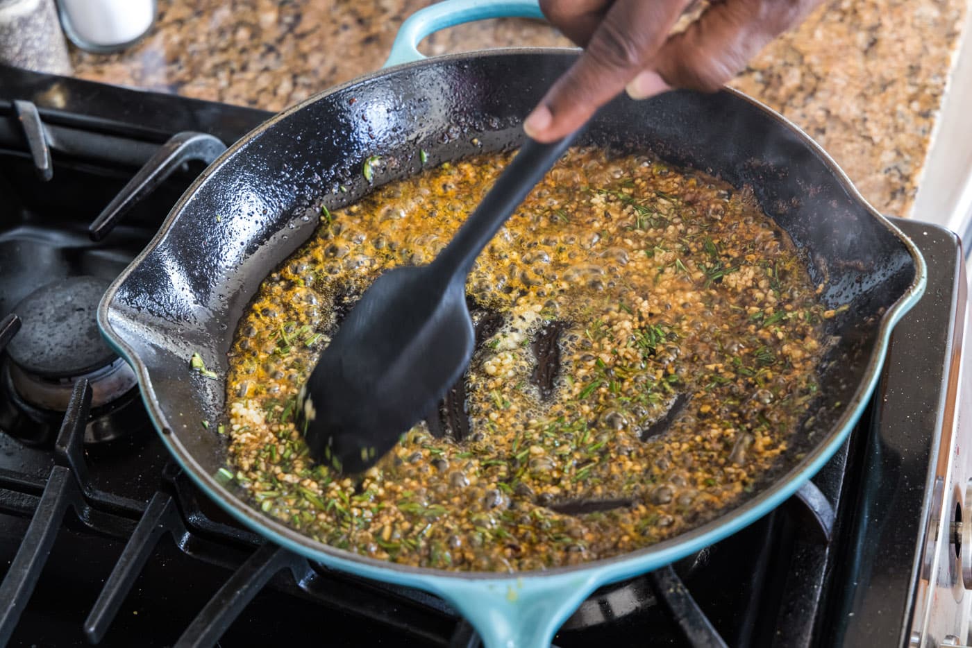 spatula mixing garlic, rosemary, butter, and oil in a skillet