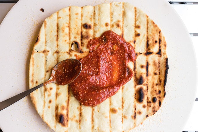 spreading sauce on grilled pizza dough