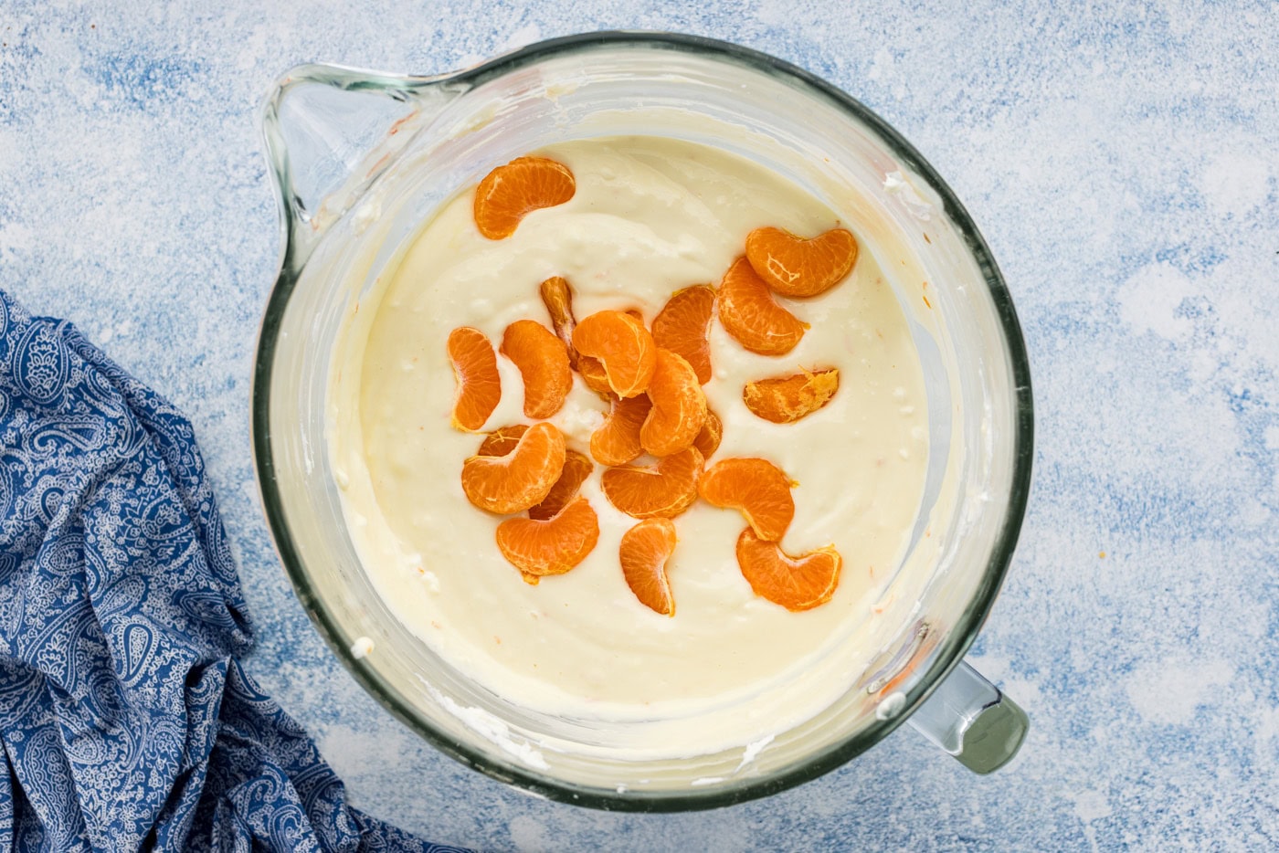 mandarin orange slices added to cheesecake batter in a bowl
