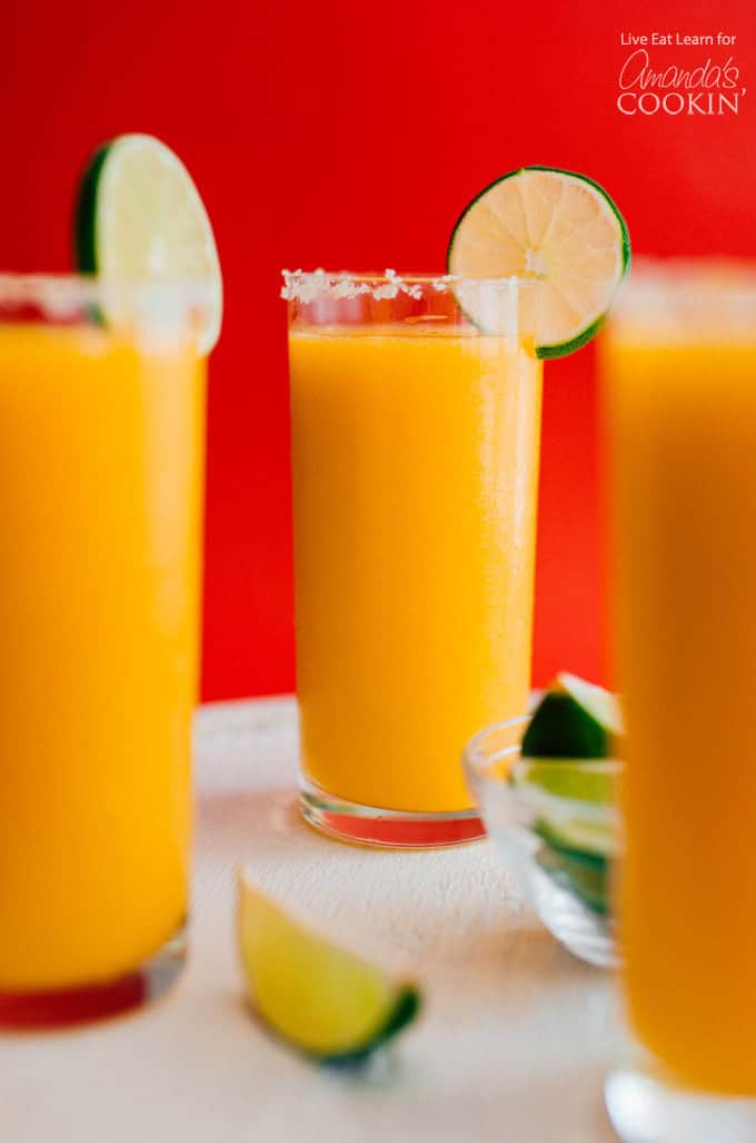 Three glasses full of mango margarita slush with a lime garnish