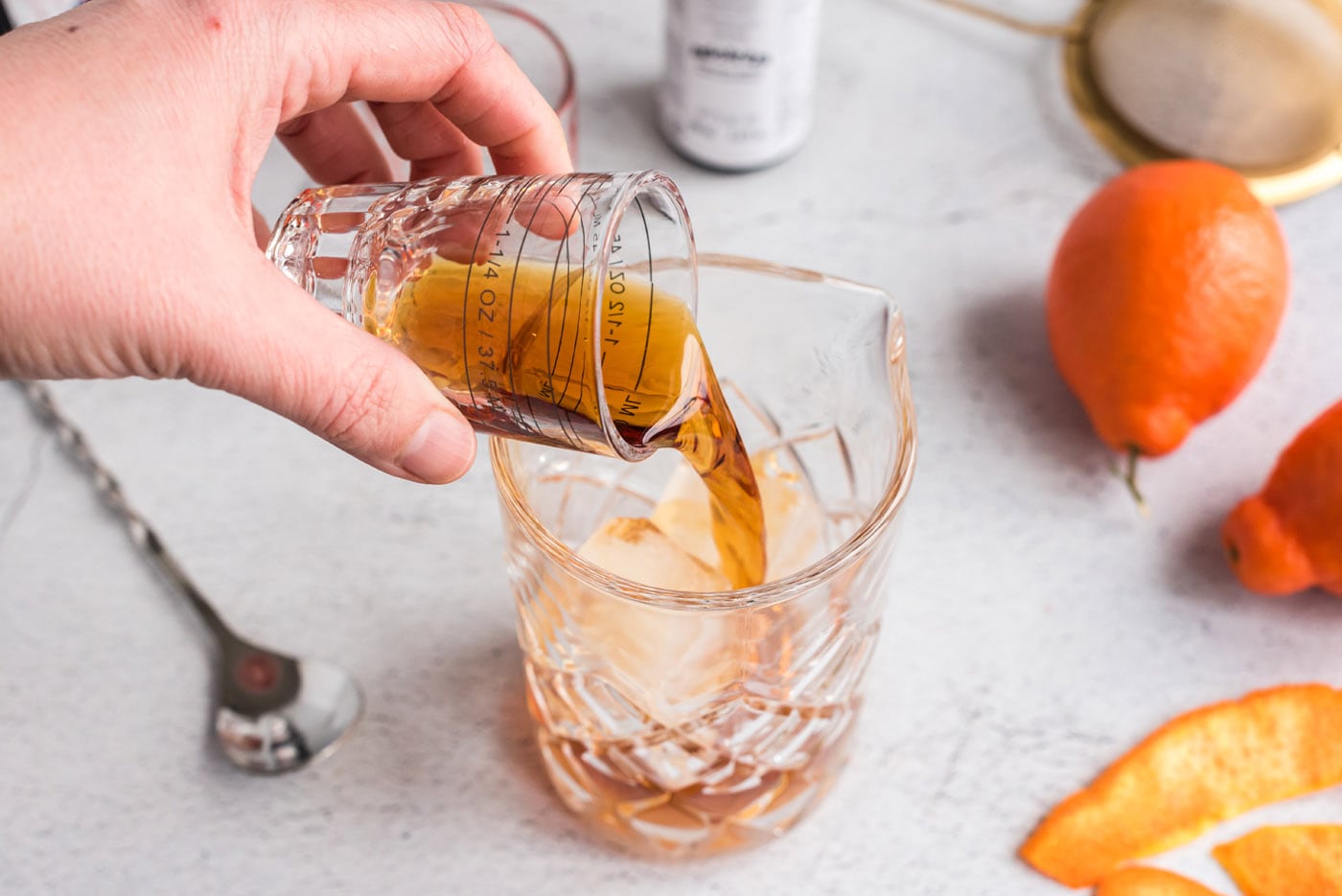 pouring whiskey and vermouth into mixing glass
