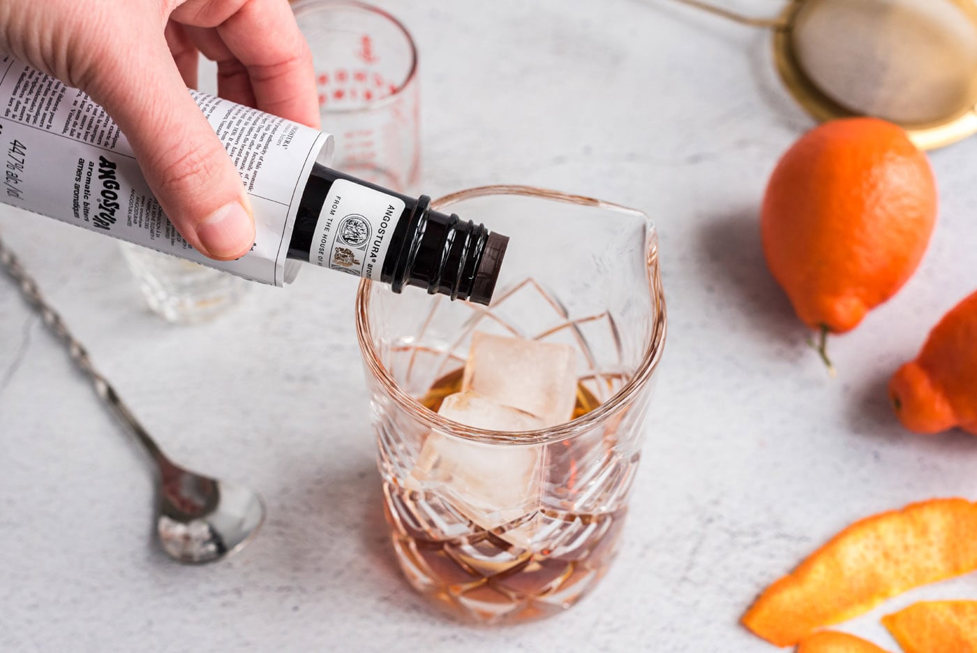 adding bitters to manhattan cocktail mixing glass
