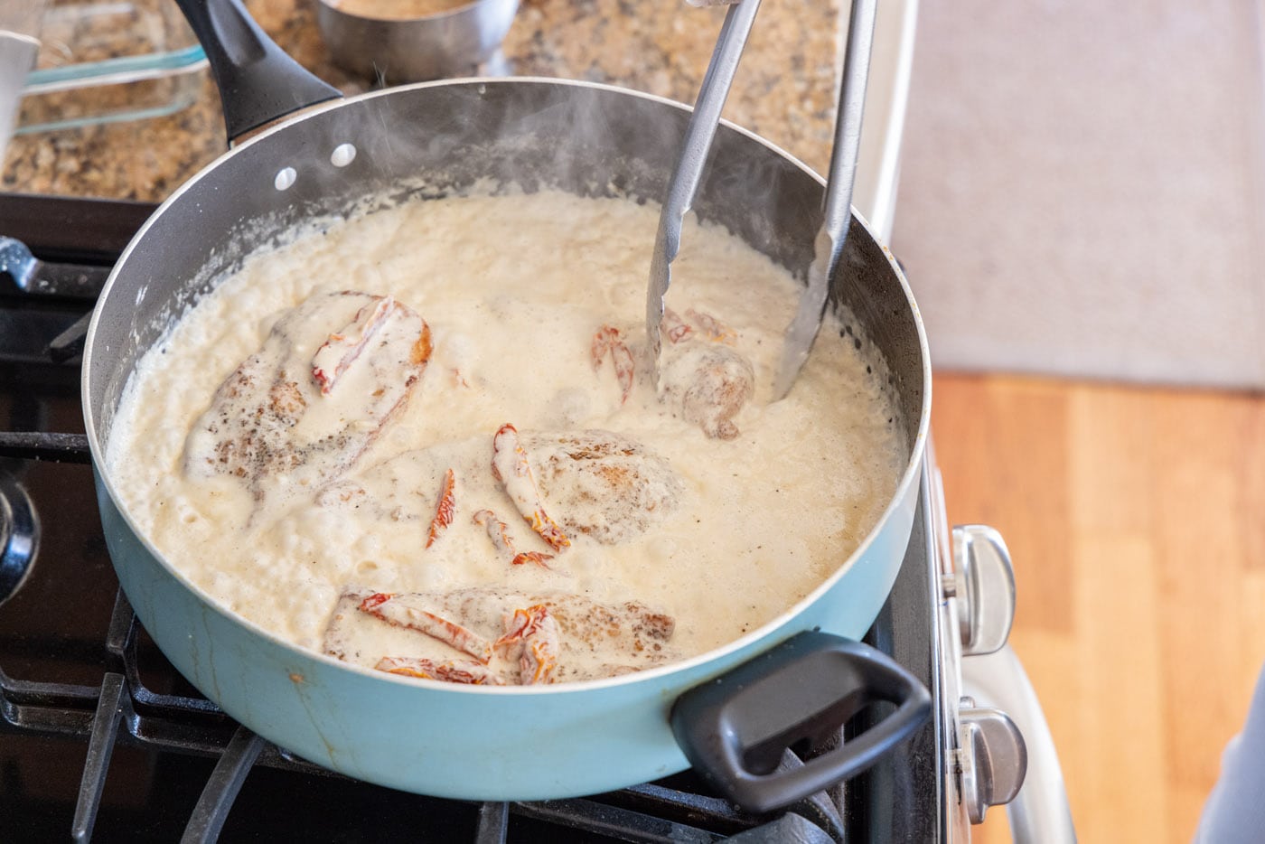 flipping chicken breasts in a skillet with heavy cream sauce