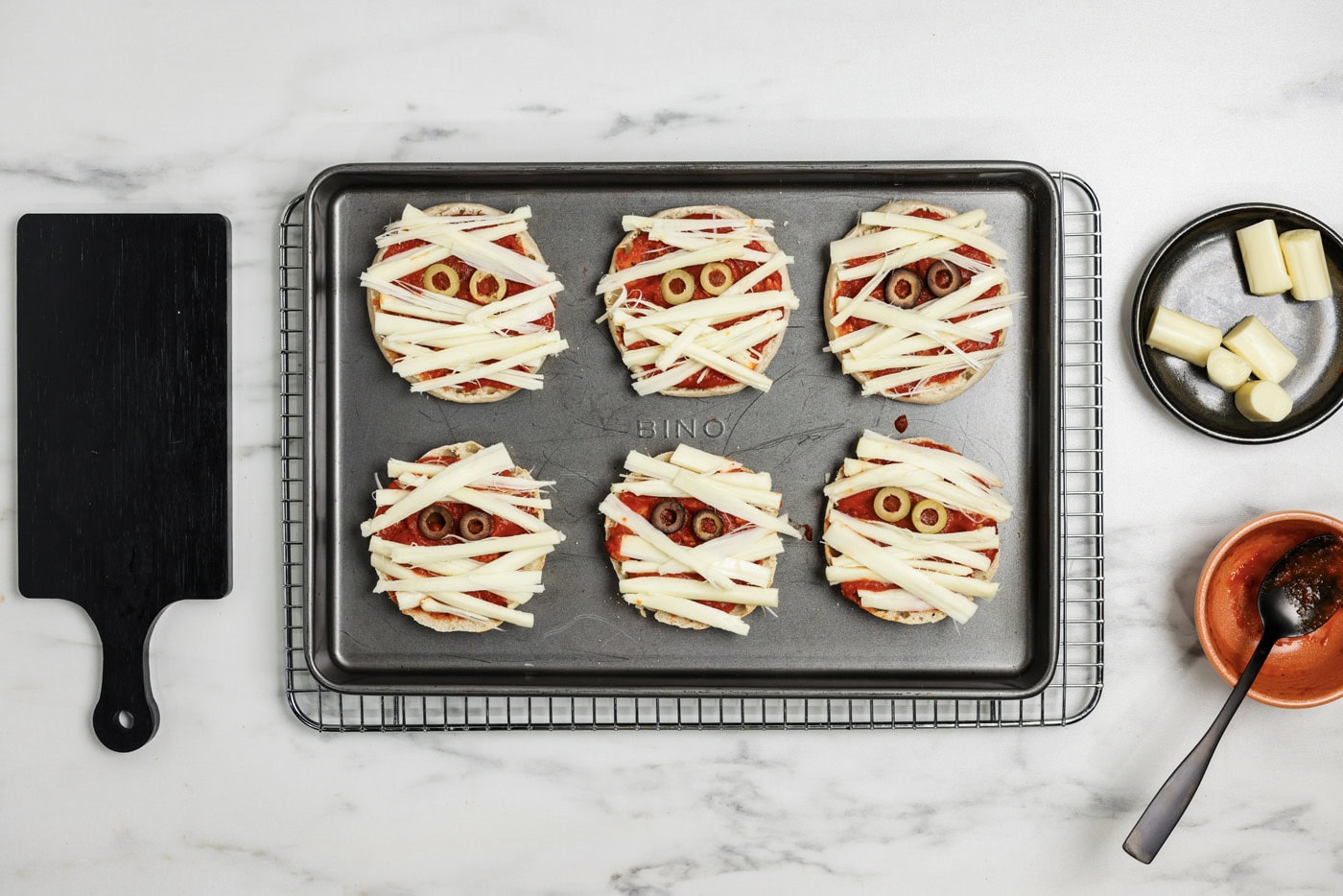 strips of cheese on top of English Muffins with sliced olive eyes to look like mummies