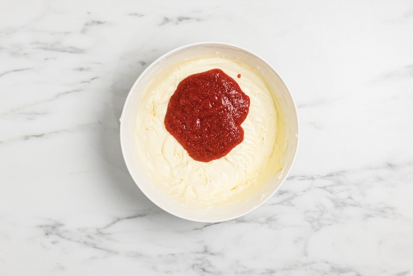 strawberry compote added to cheesecake batter in a bowl