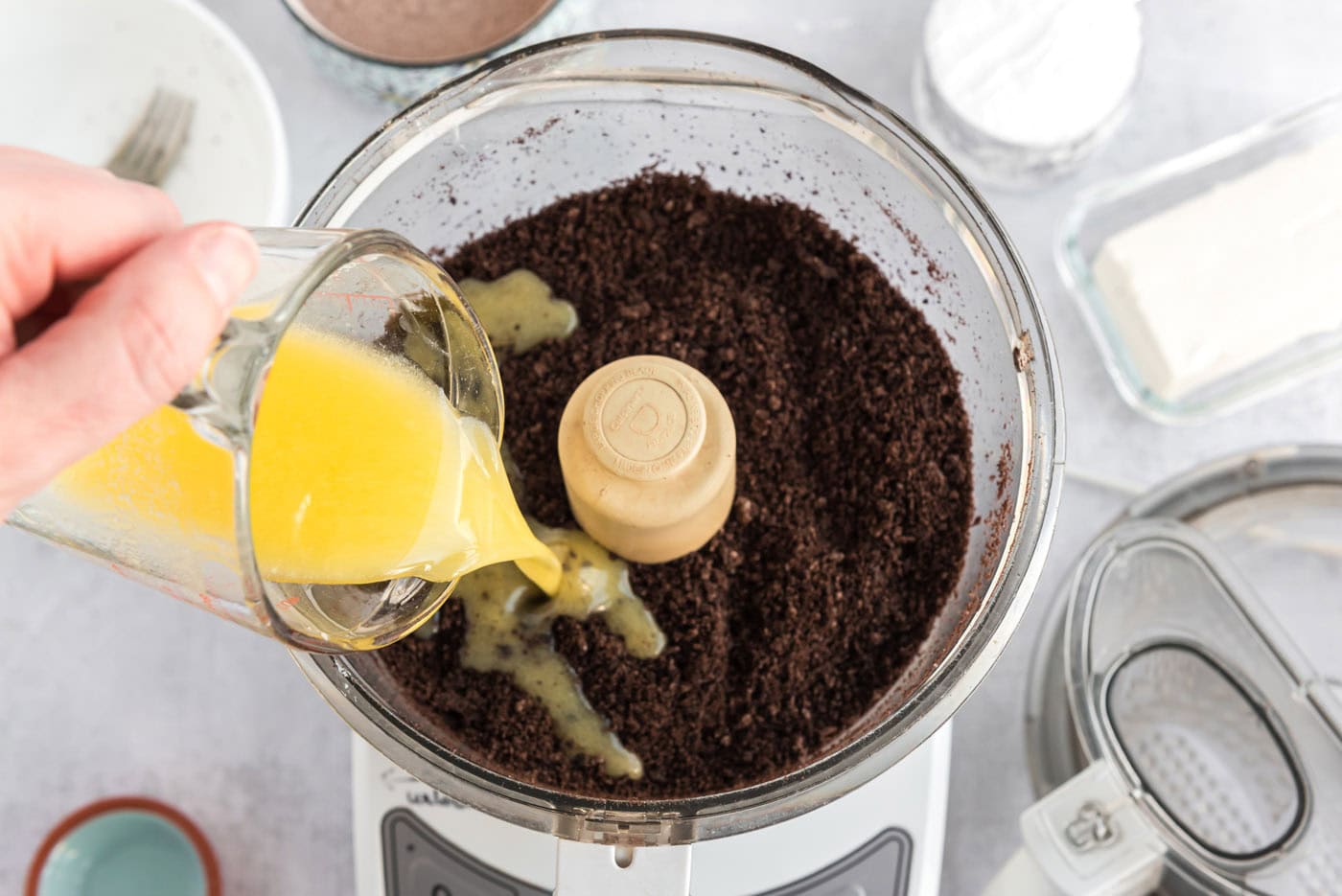 pouring melted butter over Oreo cookie crumbs in a food processor