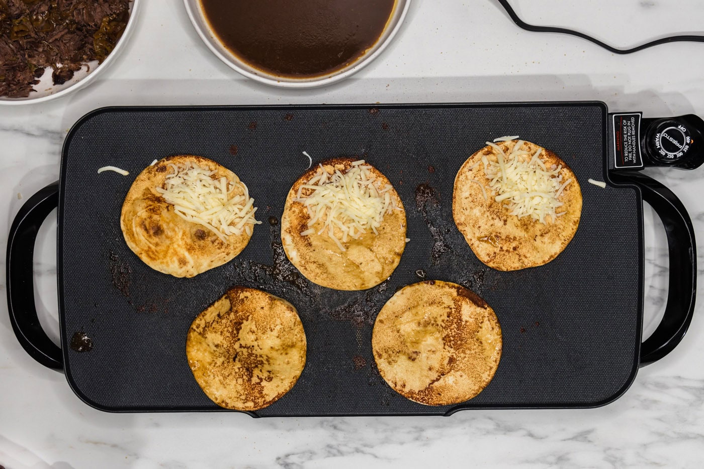 shredded cheese added to tortillas on a griddlee